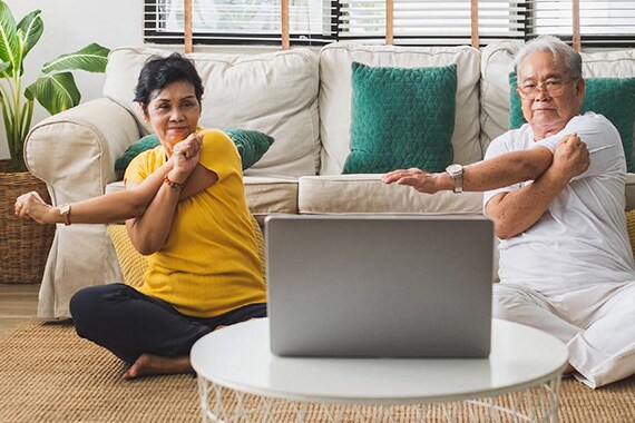 senior couple exercising with laptop in living room